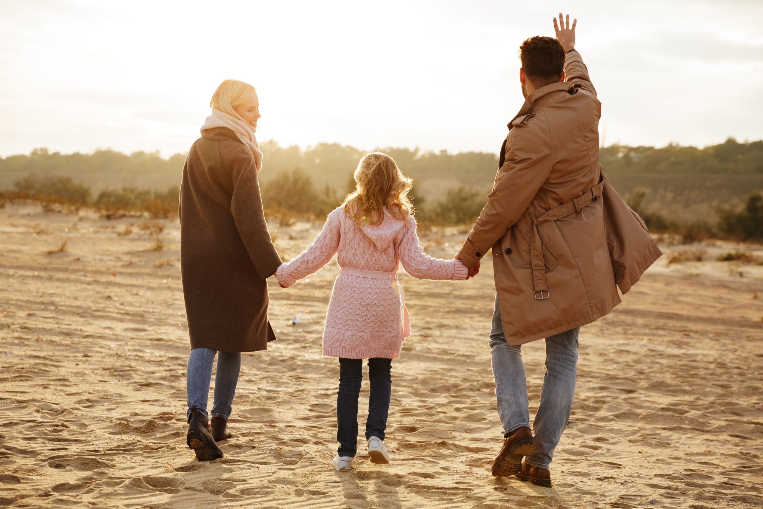Portrait of a cheerful family with a little daughter having fun while walking along the beach together holding hands
